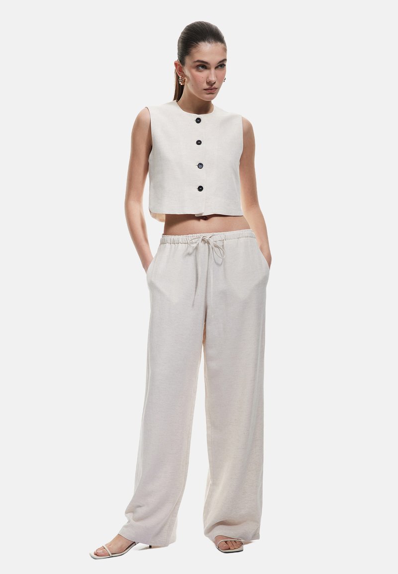 Top corto in lino chiaro con bottoni neri abbinato a pantaloni larghi con cordoncino. Tessuto morbido, vestibilità rilassata, design minimalista.