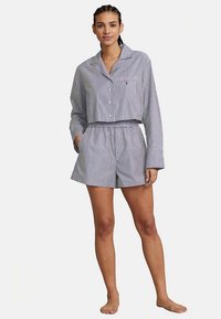 Lyhyt nappipaita ja shortsit, joissa sinivalkoraidallinen kuvio, valmistettu kevyestä kankaasta. Paidassa on taskudetalji.