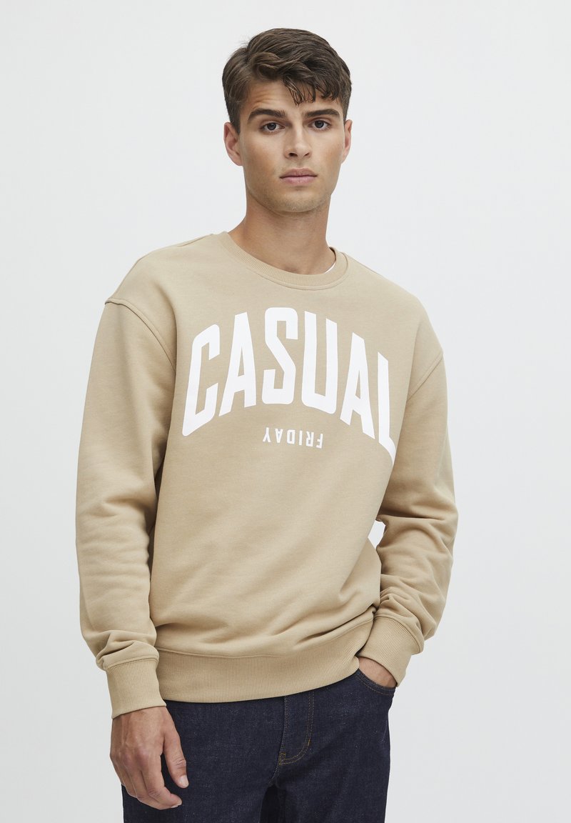 Béžová mikina s kulatým výstřihem a bílým nápisem „CASUAL FRIDAY“, se žebrovanými manžetami a spodním lemem, vyrobená z jemné, strukturované látky.
