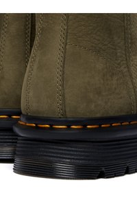 Botines de ante verde oliva con costuras naranjas contrastantes y una suela de goma negra con relieves texturizados.