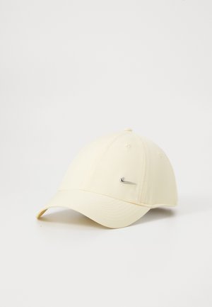 Helles beige Baseballcap mit gebogenem Schirm und einem kleinen silbernen Nike Swoosh-Logo auf der Vorderseite rechts.