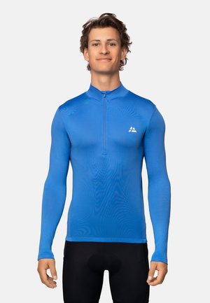 Haut de sport à manches longues bleu avec un col zippé, fabriqué en tissu lisse et léger. Il présente un petit logo blanc sur le haut à gauche de la poitrine.