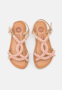 Sandalias de cuero marrón claro con un diseño de tiras de cuentas coral y un patrón troquelado. Correa ajustable en el tobillo con cierre de hebilla de metal.