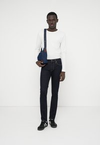 Σκούρα μπλε τζιν παντελόνια, λευκό μακρυμάνικο πουκάμισο και μαύρα αθλητικά παπούτσια. Αξεσουάρ: μικρή τζιν τσάντα ώμου με λουράκι και δερμάτινη λεπτομέρεια.