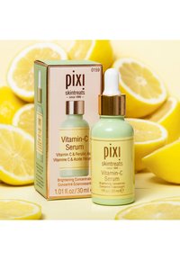 Grønn glassdråperflaske med gullhette, merket "Vitamin-C Serum." Boksen har mintgrønn og beige farger, dekorert med tekst og logoer.