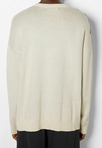 Pull en maille beige clair à coupe décontractée, poignets et ourlet côtelés. Tissu texturé, tissage ouvert sur les épaules, dos uni.