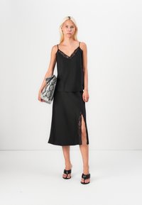 Black satin camisole with lace trim and matching midi skirt featuring a side slit, held with a grey snakeskin clutch and black sandals.