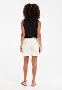 Top negro sin mangas combinado con shorts de algodón blancos. Los shorts tienen un dobladillo enrollado y dos bolsillos traseros con acentos de botones marrones.