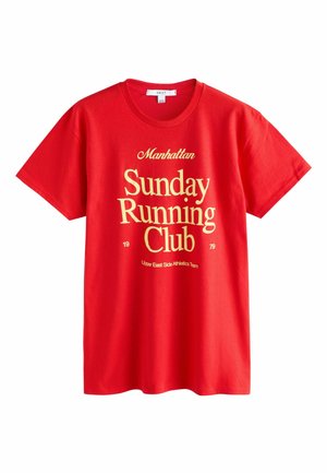 Piros, rövid ujjú póló sárga felirattal: „Manhattan Sunday Running Club 1979 Upper East Side Athletics Team.”