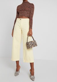 Hnědý dlouhý rukáv crop top s vzorovaným designem, žluté široké kalhoty a texturovaná kabelka vzorovaná hadí kůží. Texturované lodičky na vysokém podpatku.