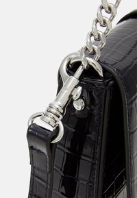 Coin de sac en cuir noir texturé crocodile avec une chaîne en argent et un matériel de fermeture attaché à une boucle de sangle en cuir.