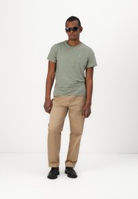 Camiseta de manga corta a rayas verdes, pantalones caqui y zapatos negros. La camiseta presenta un pequeño logo, textura suave y un corte casual.
