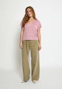 Top rosa chiaro a maniche corte con scollo a V e finitura testurizzata, abbinato a pantaloni morbidi verde oliva e tacchi beige a punta.