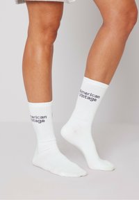 Calcetines de algodón blancos con diseño acanalado, con "American Vintage" impreso en gris en un lado. Textura suave, longitud a medio pantorrilla.