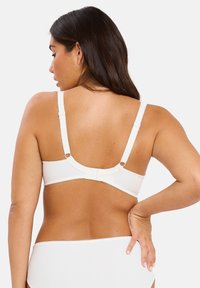 Bralette blanco acanalado con tirantes ajustables, cierre de gancho y ojal en la parte posterior, y un borde con ondas a lo largo de los bordes. Diseño simple y sin costuras.