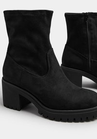 Czarne zamszowe botki za kostkę z okrągłym noskiem, grubym obcasem i teksturowaną gumową podeszwą. Posiadają boczny zamek błyskawiczny ułatwiający zakładanie.