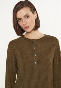 Olivgrüner, gerippter Pullover mit rundem Halsausschnitt, langen Ärmeln und einer Knopfleiste mit vier Knöpfen. Strukturiertes Gewebe mit leichtem Schimmer.