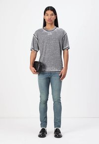 Grå, kortermet T-skjorte med teksturert finish, brukt sammen med lyseblå jeans og svarte sko. En liten svart veske holdes i den ene hånden.