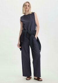 Toppia ilmanhihoja navy raidallinen, rento istuvuus, yhdistetty leveälahkeisiin navy raidallisiin housuihin. Neulottu neuletakki on solmittu vyötärölle.