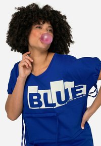 Blauwe T-shirt van zachte stof, met korte mouwen met trekkoorden, een groot wit tekstontwerp en een voorzak.