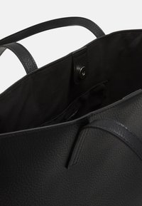 Czarna skórzana torba na ramię o teksturowanej powierzchni, z dwoma uchwytami i zapięciem na zatrzask. Wnętrze wyłożone czarnym materiałem.