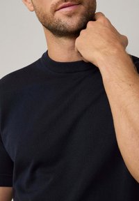 Mørk navy kortærmet t-shirt med ribbet rund halsudskæring, lavet af glat, let materiale, der viser diskrete tekstur- og pasformdetaljer.
