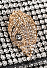 Broche doré à la conception complexe, ornée de strass clairs et foncés, sur fond de strass noirs.