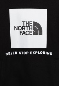 Felpa nera con un quadrato bianco contenente un logo circolare e il testo "THE NORTH FACE" sopra a "NEVER STOP EXPLORING" in grassetto bianco.