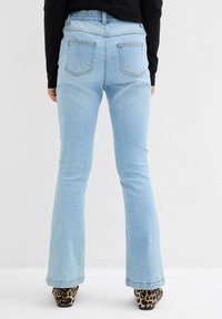 Jeans a zampa d'elefante di un blu chiaro con vita alta e retro elasticizzato. Quattro tasche visibili. Accentati da una leggera texture sbiadita.