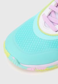 Zapatilla deportiva azul claro con parte superior de malla, cuello acolchado y detalles en tonos pastel. Suela texturizada con realces en rosa y amarillo.