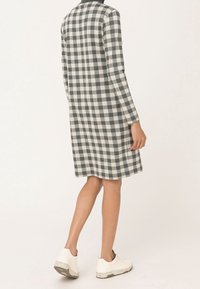 Robe à carreaux grise et blanche avec des manches longues, longueur genou, fabriquée dans un tissu doux. Associée à des chaussures blanches avec une semelle texturée.