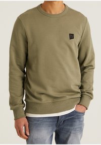 Felpa verde oliva in misto cotone, con scollo rotondo e polsini a costine, con una piccola patch logo nera sulla parte superiore sinistra.