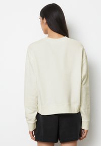 Felpa beige chiaro con scollatura tonda, spalle abbassate e polsini a coste. Scollo aderente in vita, realizzata in morbido tessuto testurizzato.