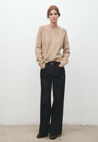 Suéter de punto beige con patrones texturizados, combinado con pantalones de mezclilla oscuros de pierna ancha de cintura alta y un cinturón negro con hebilla dorada.