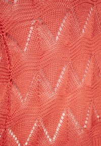 Korallenfarbener Strickstoff mit einem Zickzackmuster und offenen Maschen. Die Textur ist leicht und luftig, ideal zum Schichten.