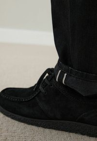 Svart mockaskor med snören, med en texturerad sula. Kombinerad med uppvikta svarta jeans, med kontrasterande sömmar.