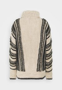 Beige neulepusero korkealla kaulalla, jossa on mustia teksturoituja raitoja ja fringed-yksityiskohtia sivuilla ja hihoissa. Paksu neuletekstuuri.