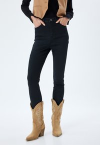 Jeans ajustados negros de talle alto, combinados con botas de vaquero de ante color tostado que presentan un bordado intrincado y puntas afiladas.