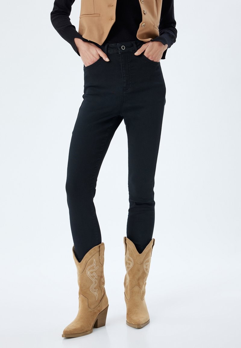 Jeans ajustados negros de talle alto, combinados con botas de vaquero de ante color tostado que presentan un bordado intrincado y puntas afiladas.