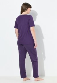 T-shirt di cotone viola con maniche corte e scollatura a contrasto, abbinata a pantaloni pigiama viola coordinati con un motivo a pois bianchi.