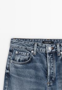 Jeans in denim blu con una finitura sbiadita, con un classico design a cinque tasche, rivetti in metallo e una etichetta cucita nella cintura.