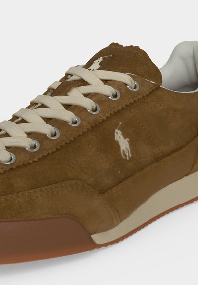 Baskets en daim marron avec lacets blancs, logo cheval blanc sur le côté et la languette, et semelle blanche et marron.