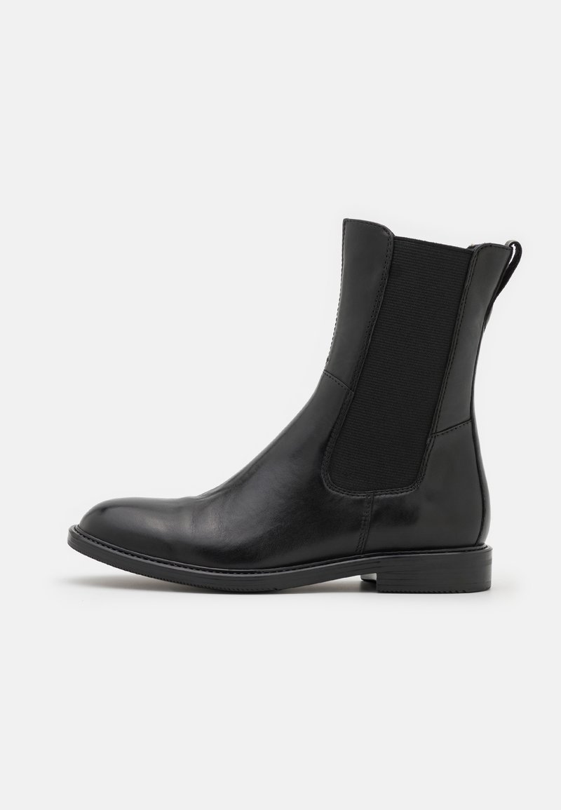 Bottine Chelsea en cuir noir avec panneau latéral élastique et petit talon, montrée de profil sur un fond clair uni.