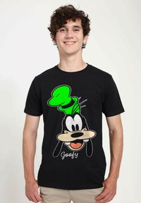 Černé tričko s grafikou karikaturního psa se zeleným kloboukem. Design zahrnuje obličejové rysy a text "Goofy" pod ním.