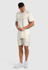 Ljus beige sporttröja med texturerad yta och subtil logotyp, matchad med beige shorts och vita sneakers.