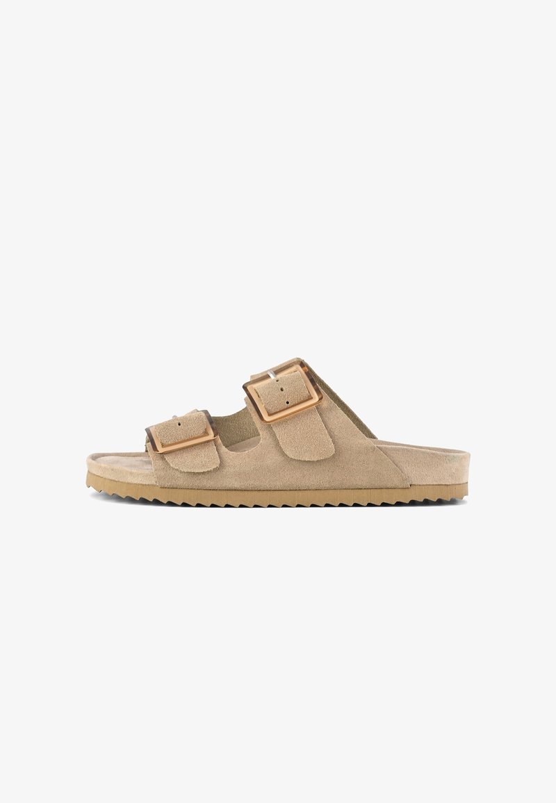Beige suede slide sandal with dual adjustable buckles, textured upper, and a thick, ridged rubber sole for grip and comfort.