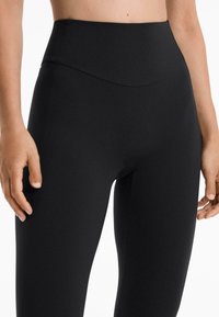 Leggings noirs taille haute en matériau extensible, avec une texture lisse, un design moulant et une silhouette élancée.