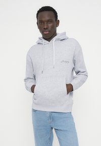 Ανοιχτό γκρι φούτερ με κουκούλα, κορδόνια και μεγάλη τσέπη τύπου καγκουρό, κατασκευασμένο από απαλό ύφασμα. Διαθέτει κέντημα λογότυπου στο στήθος και ριμπ μανσέτες.