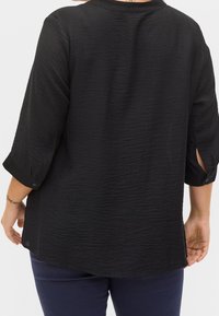 Blusa nera in tessuto strutturato con maniche a tre quarti e polsini bottone, caratterizzata da una vestibilità comoda e un orlo curvo per un maggiore comfort.