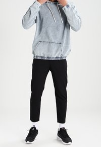 Denim-Hoodie mit einer Vorderentasche, hellblaue Farbe, elastischer Bund. Kombiniert mit schwarzen, schmal zulaufenden Hosen und schwarzen Turnschuhen.